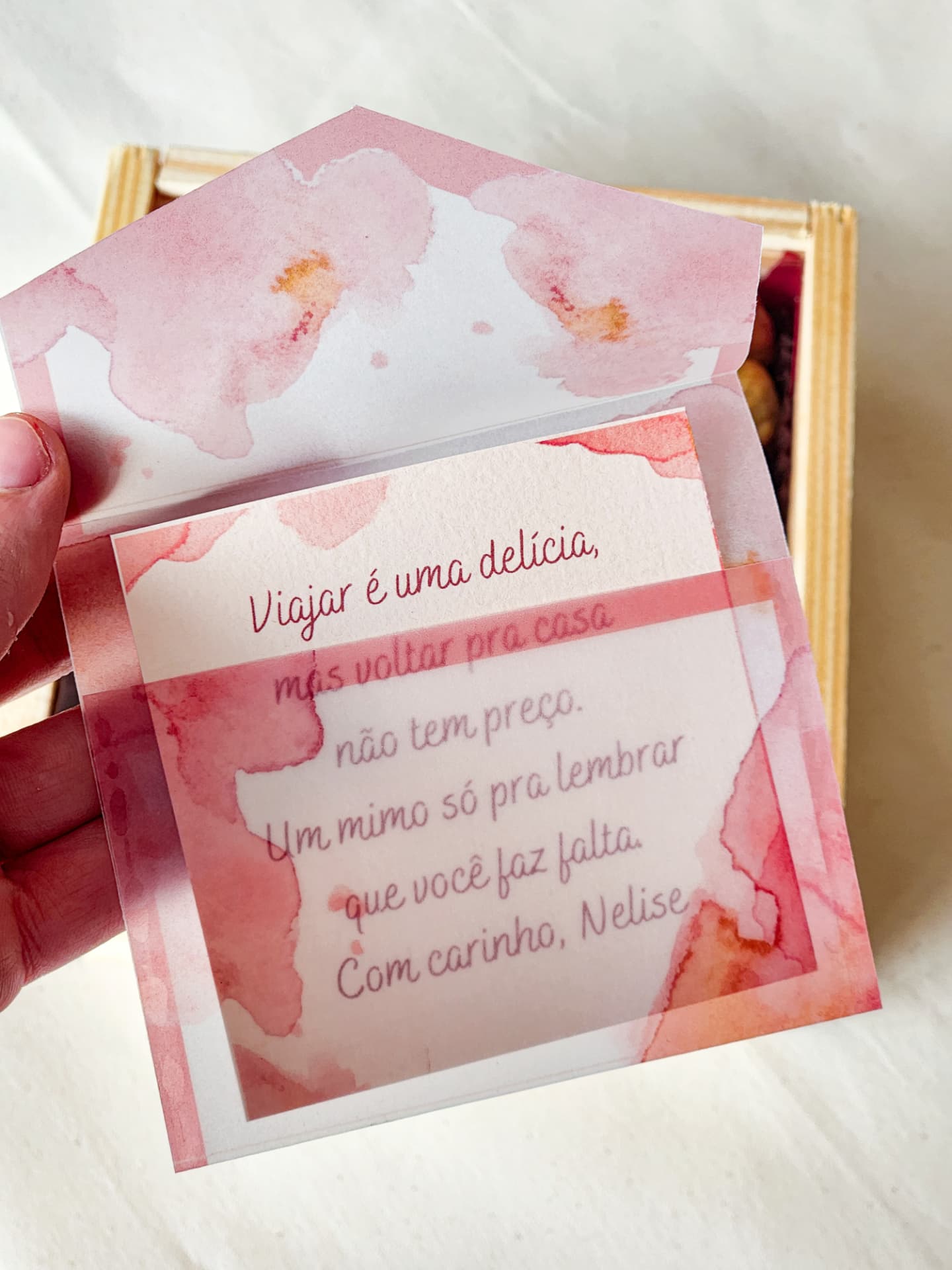 Caixa Petit Delicadezas fechada com fita, ao lado do cartão personalizado com o nome do presenteado
